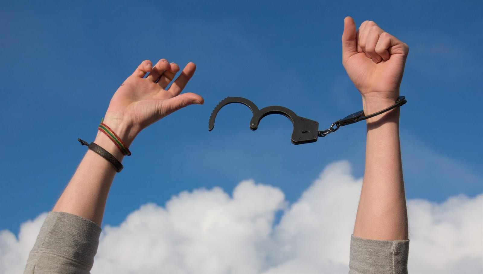 Raised hands breaking free from handcuffs against a blue sky