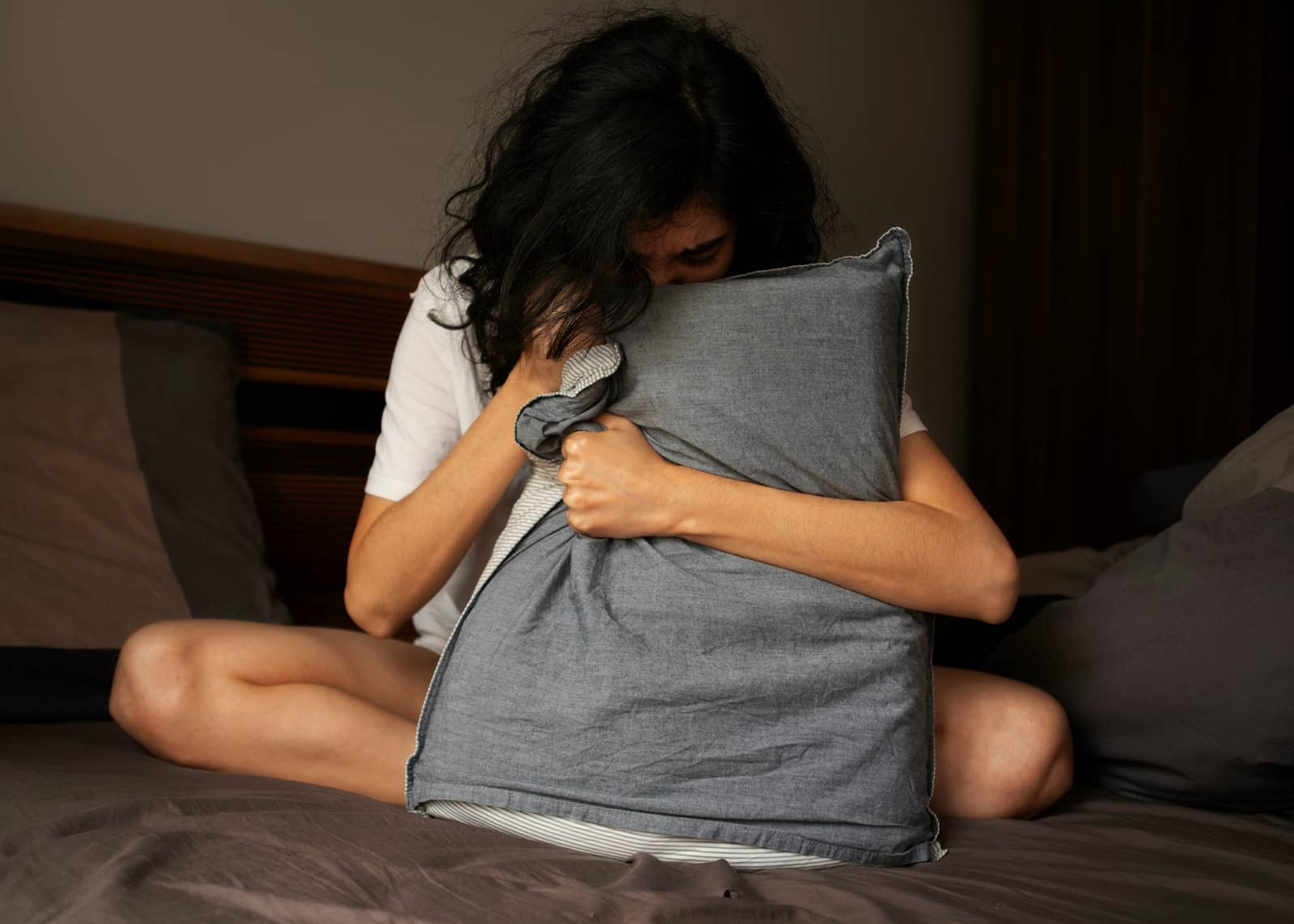 Woman sitting on a bed and holding a pillow while experiencing anxiety