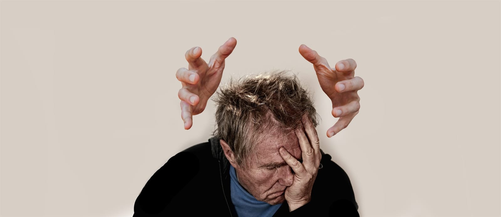 Distressed man holding his head beneath looming hands