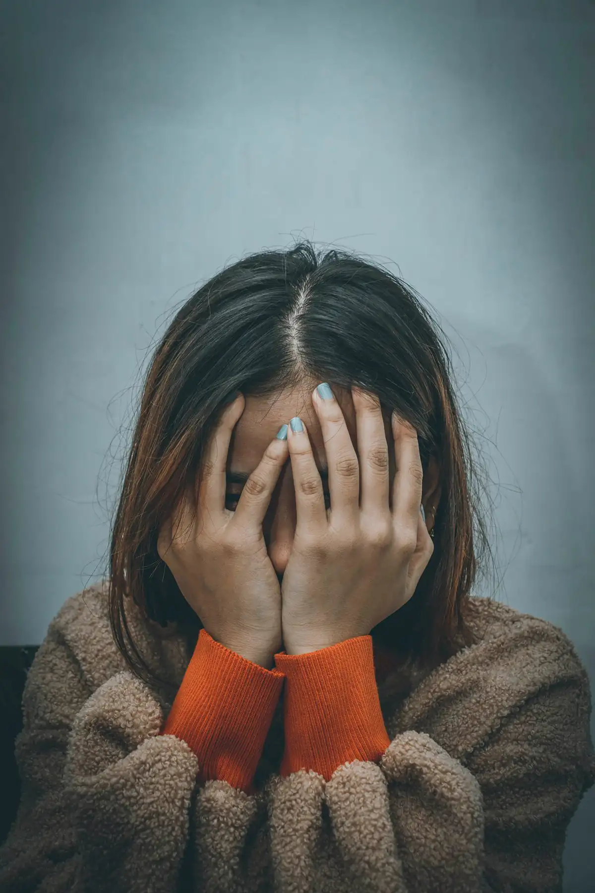 Distressed person covering their face beneath a blurred double-exposure silhouette