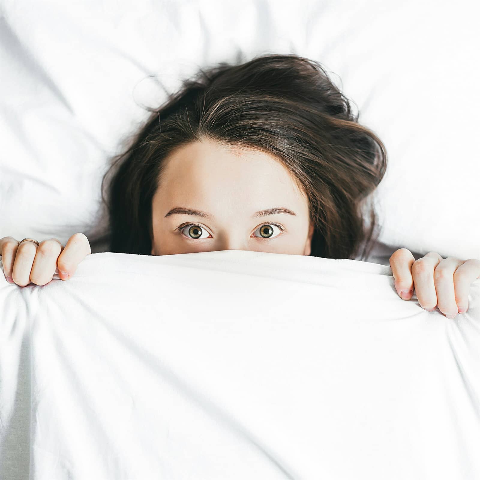 Woman lying awake and peeking over a white blanket
