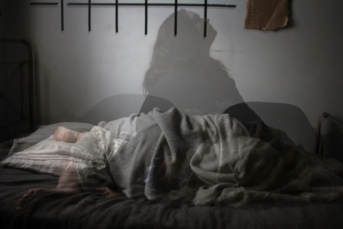 Person lying awake in bed with a shadowy sleepless silhouette behind them