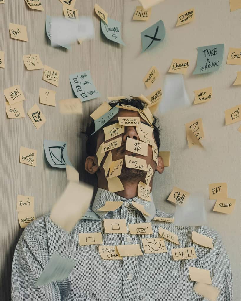 Overwhelmed person lying beneath a collection of task reminder notes